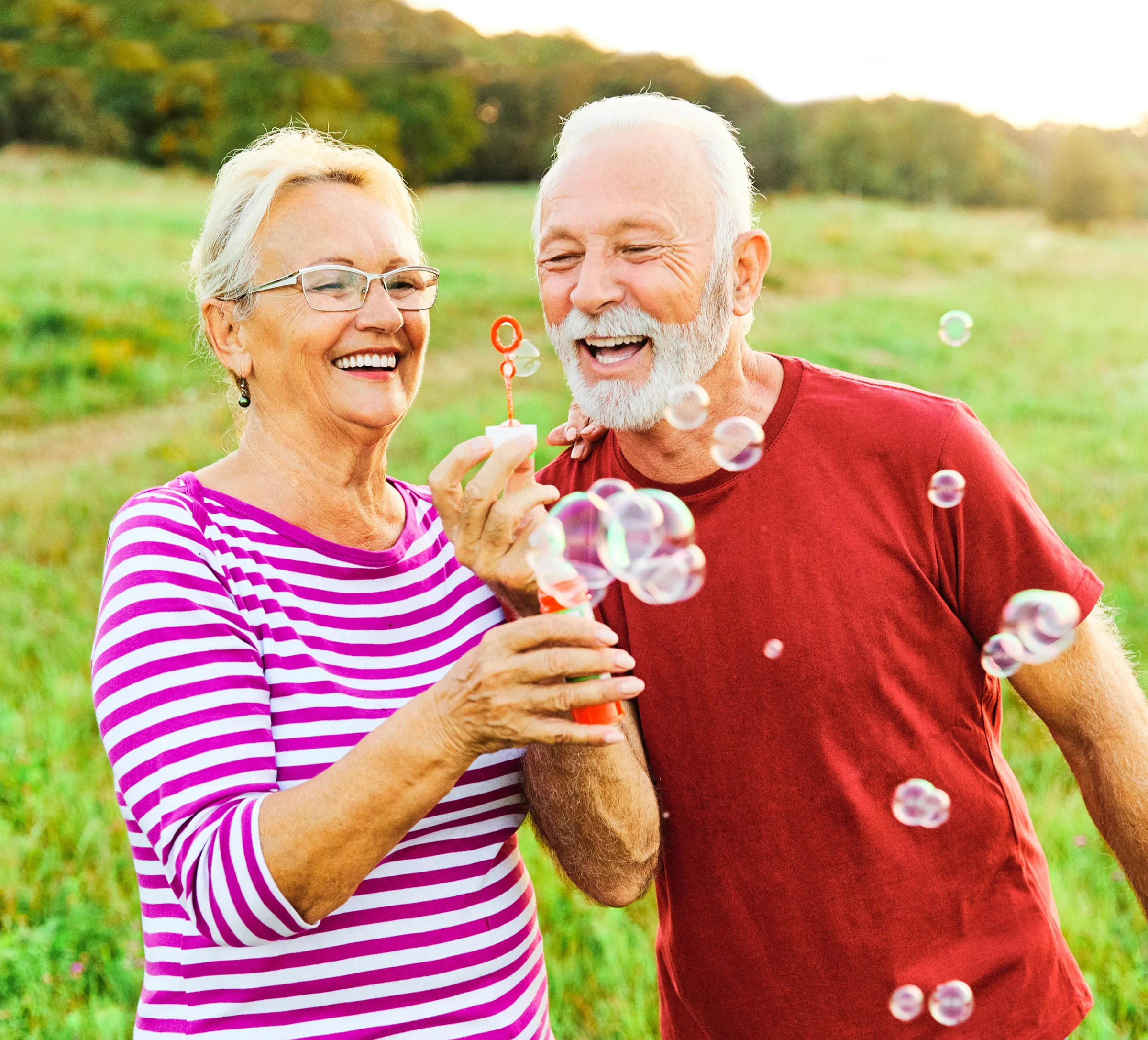An Assisted Living couple blowing bubbles in a field together.