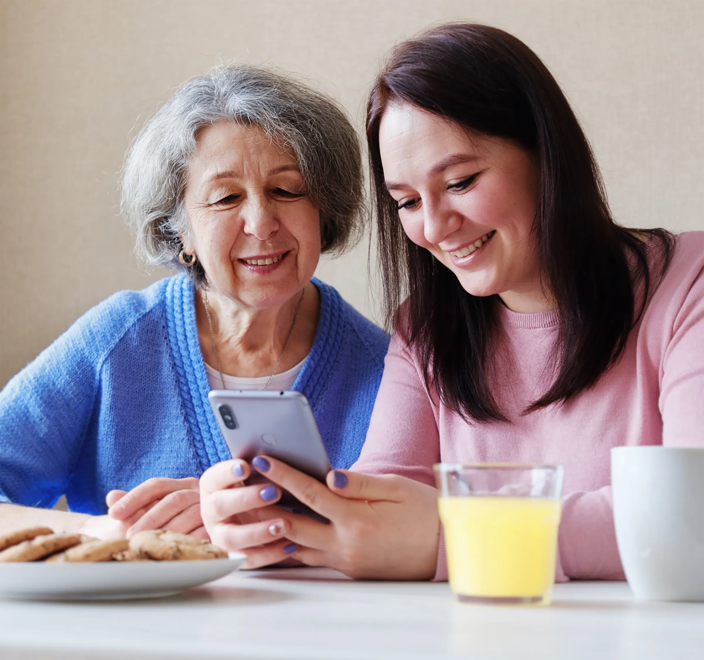 A female resident sitting at a table with her granddaughter looking at a smartphone.