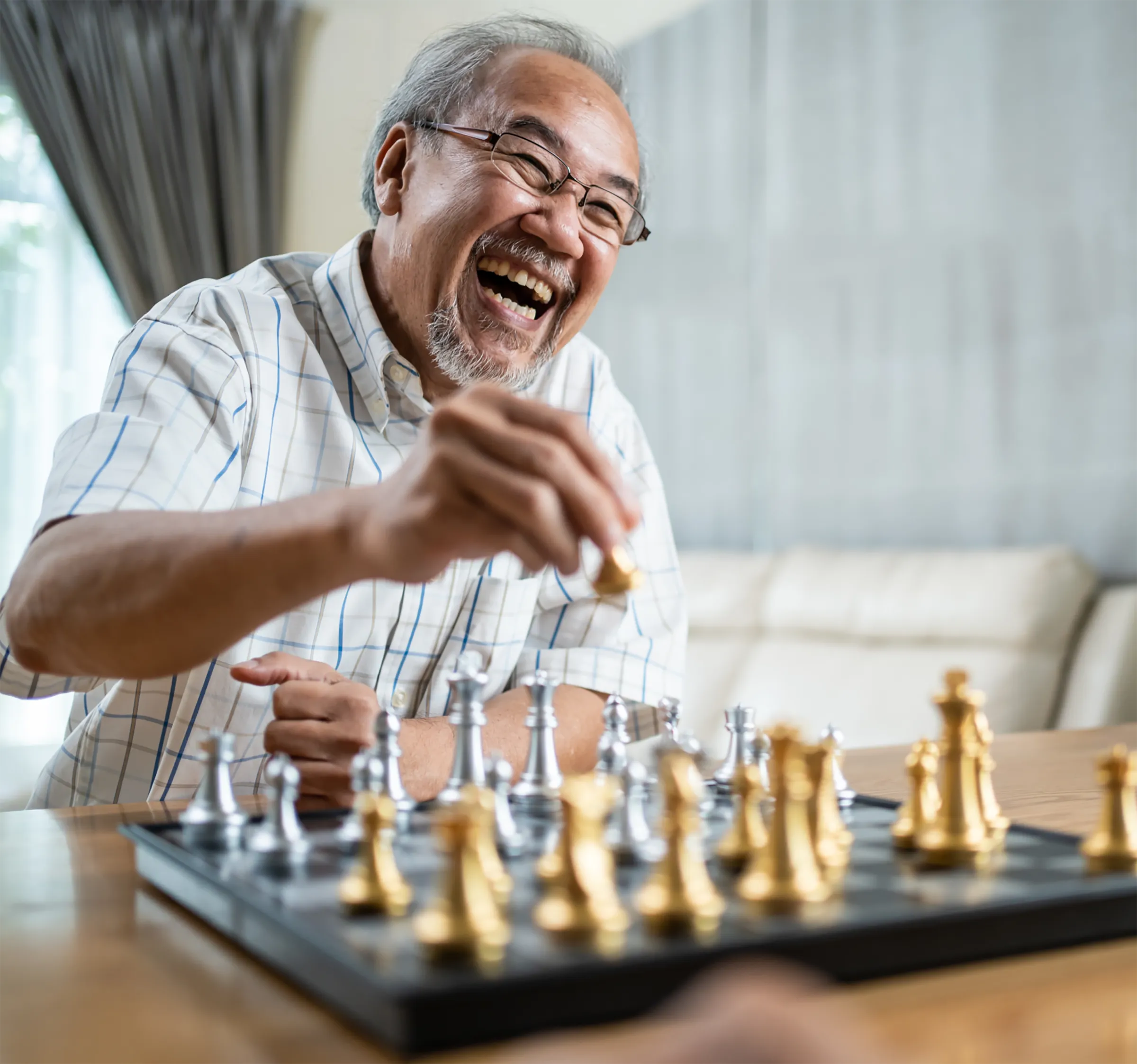 A male resident smiling and playing chess opposite his opponent.
