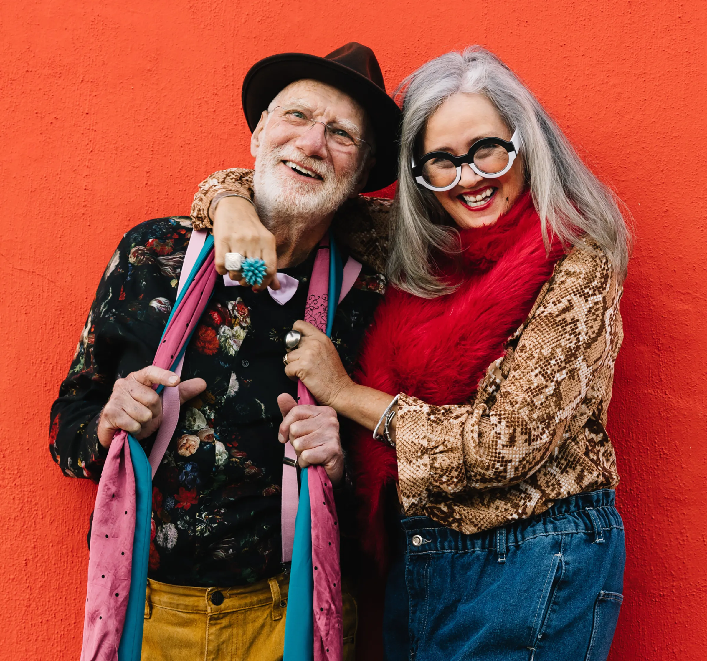 A Memory Care couple wearing loud colors and patterns posing in front of a bright orange wall.