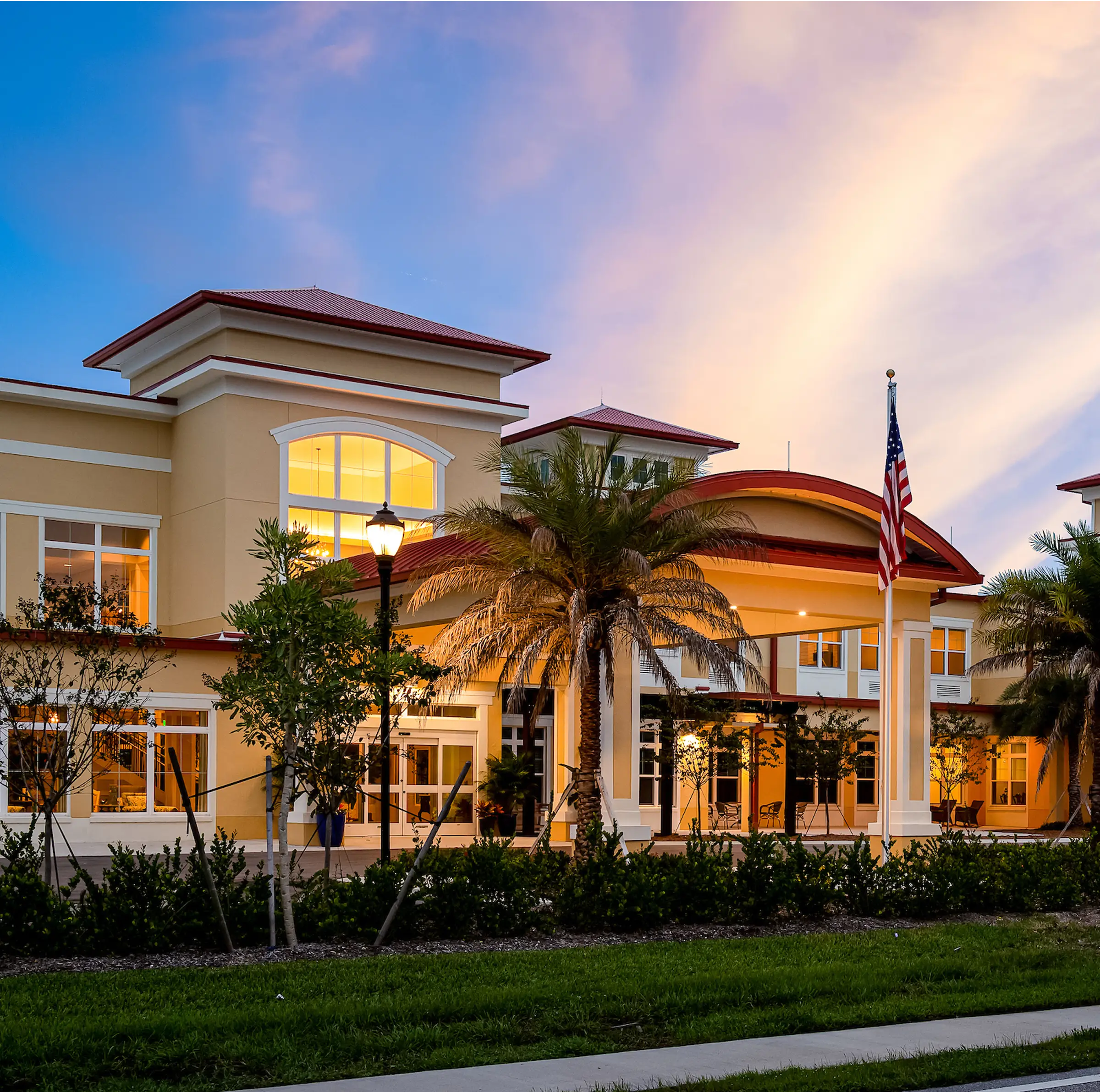 street view of yellow stucco senior living community with american flag and palm trees